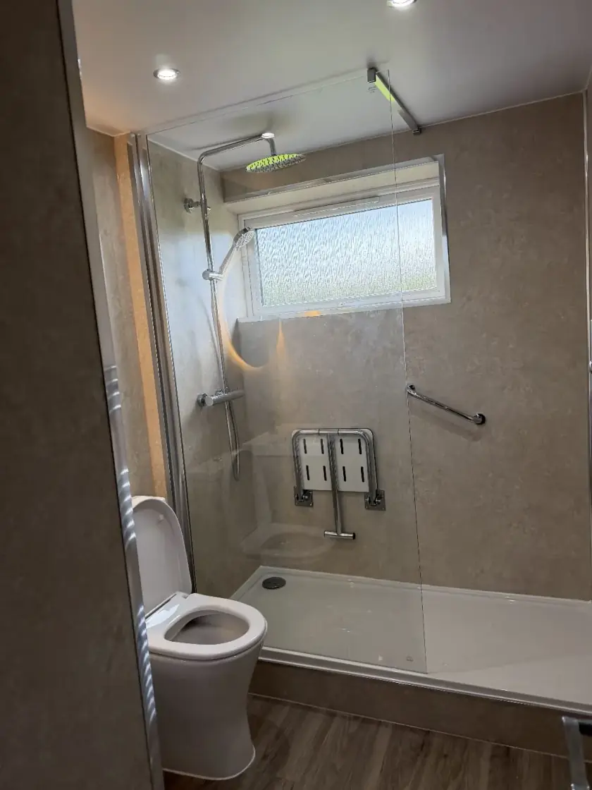 Accessible shower with neutral wet-wall panels, grab rail and fold-down seat