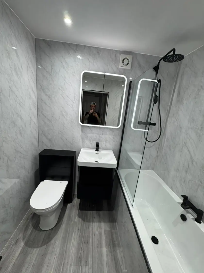 Modern grey wet-wall bathroom with black vanity, black toilet and shower over bath