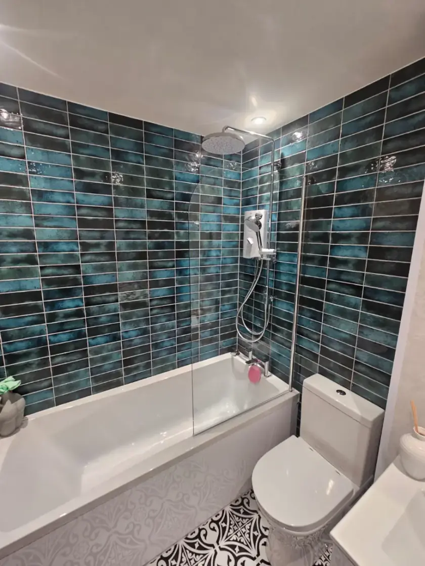 Traditional bathroom with deep blue wall tiles, shower over bath and patterned flooring