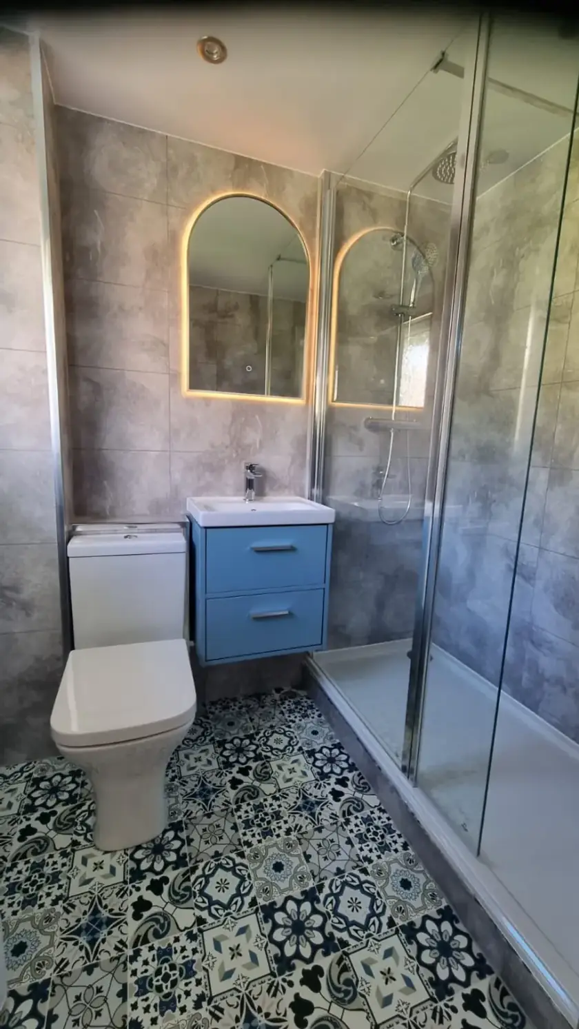 Compact en-suite with blue vanity, illuminated mirror and glass shower enclosure