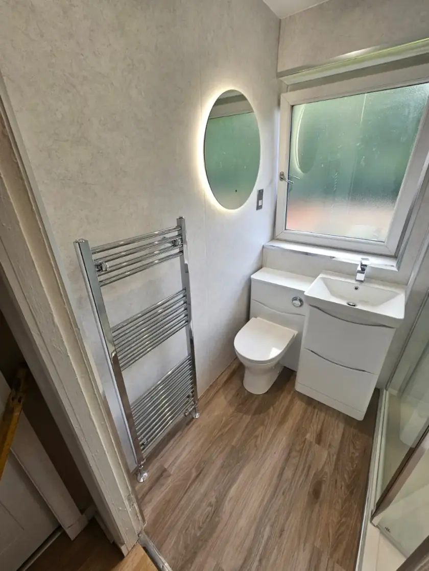 Small en-suite bathroom with white vanity, toilet, wood-effect floor and heated towel rail