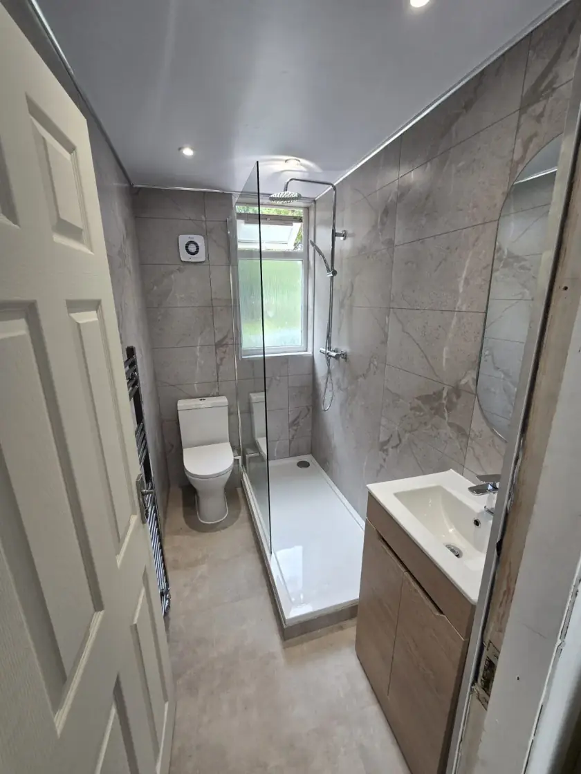 Bathroom installation with grey marble-effect panels, walk-in shower, toilet and vanity
