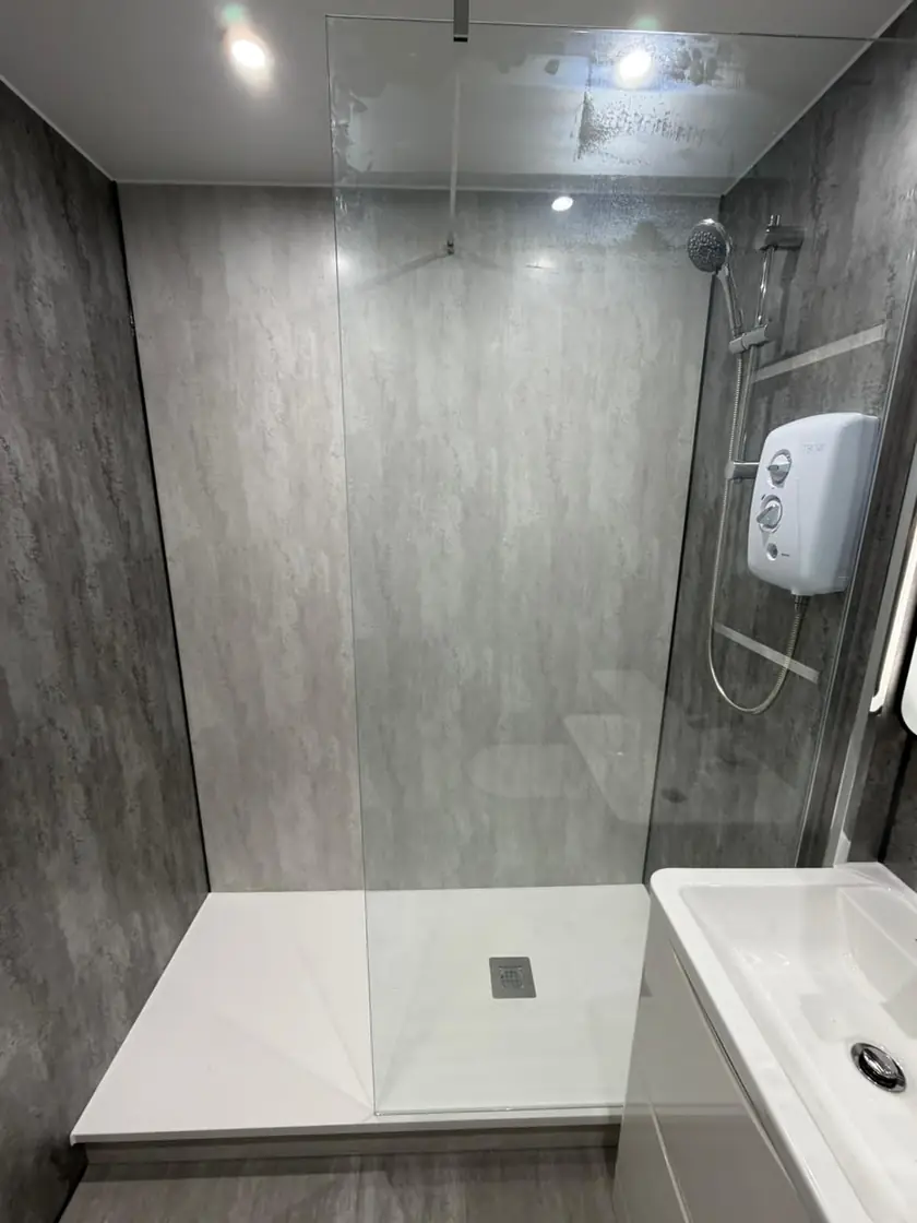 Walk-in shower with grey wet-wall panels, clear glass screen and electric shower