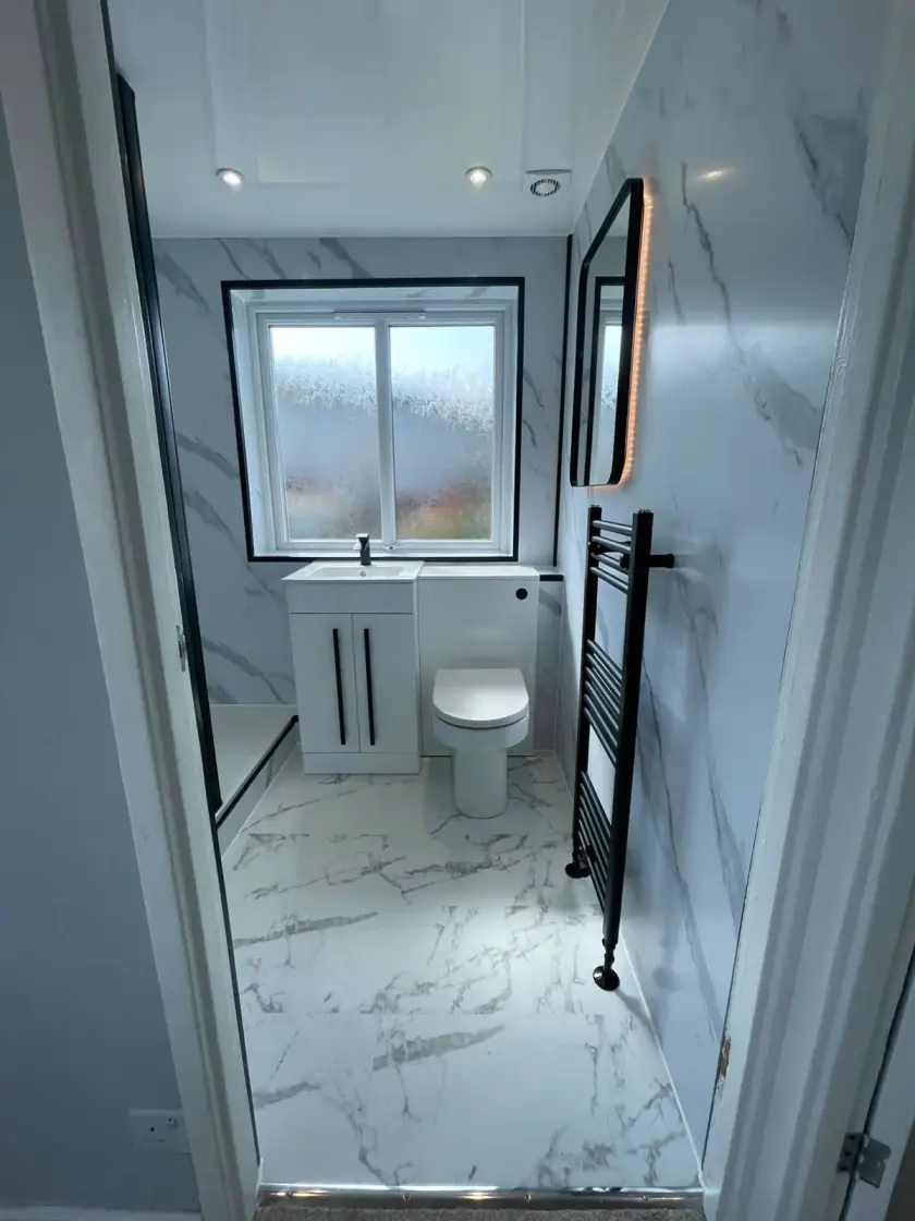 Bright marble-effect bathroom with black heated towel rail and compact vanity