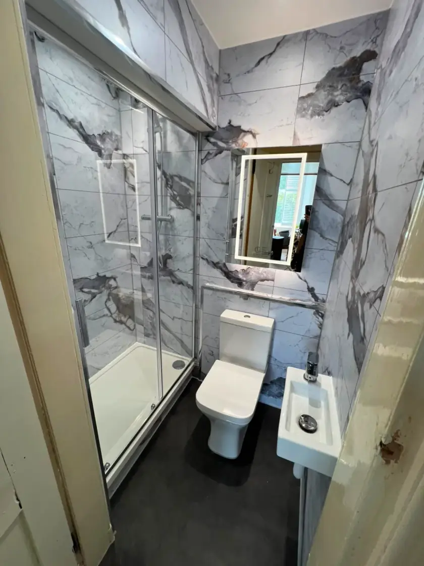 Shower room with marble-effect wall panels, white vanity and black framed mirror