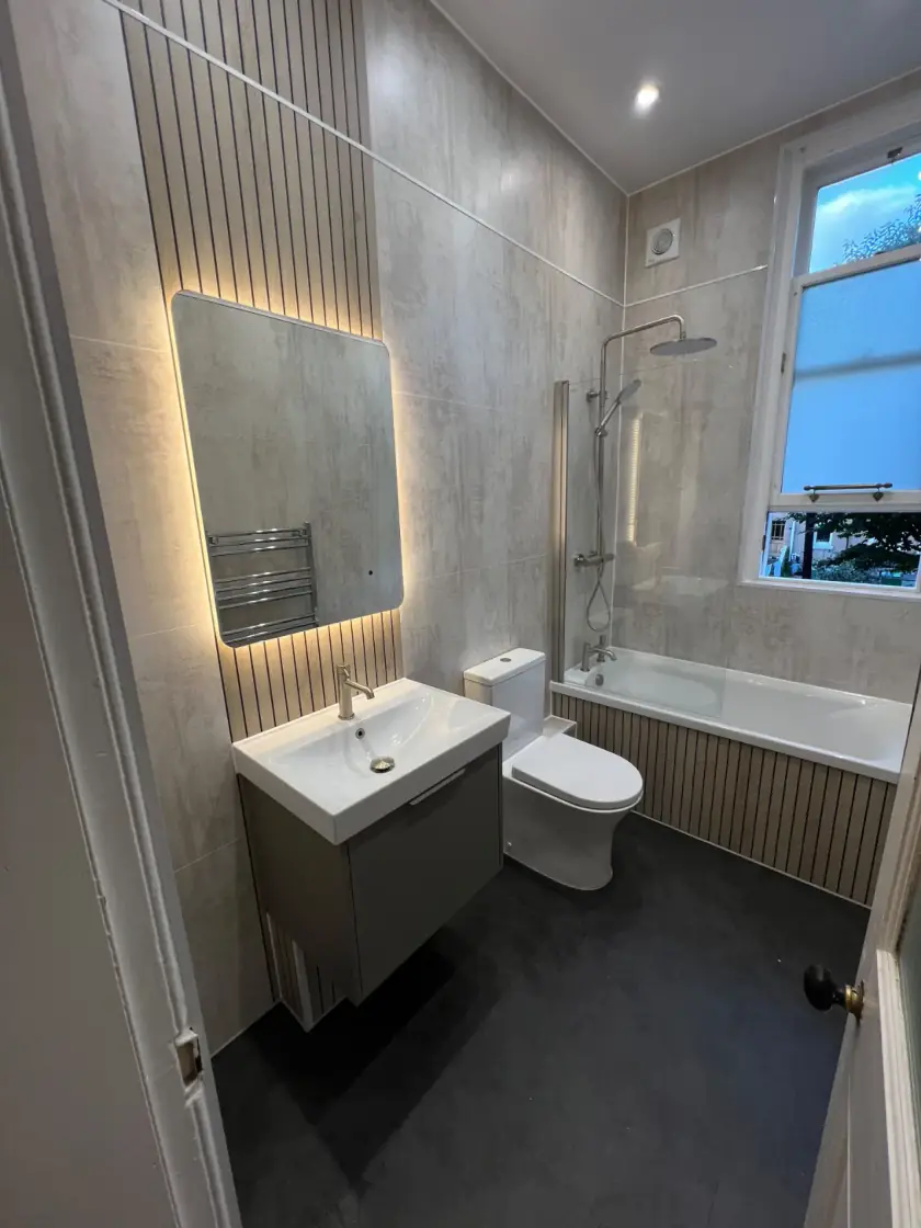 Modern bathroom with illuminated mirror, vertical wood feature wall and tiled bath panel