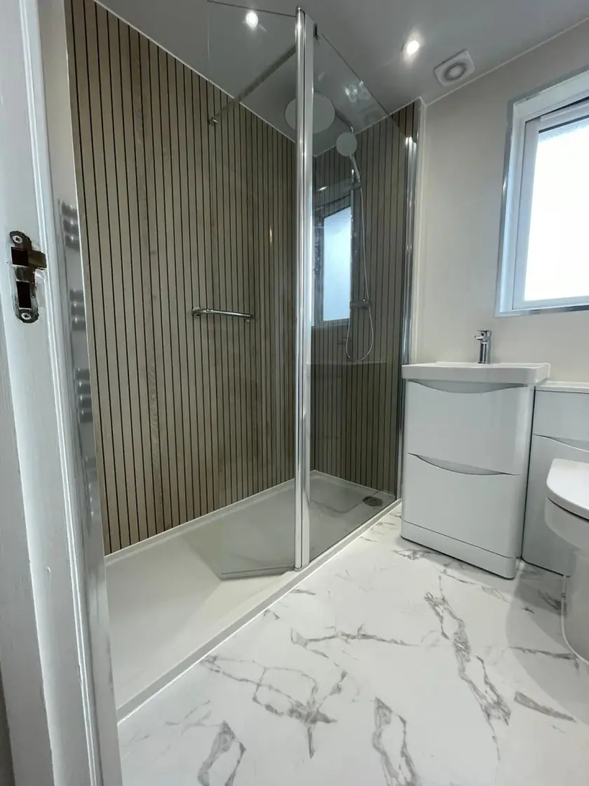 Walk-in shower with striped wet-wall panels, clear glass screen and compact vanity