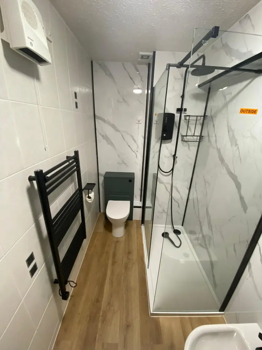 White bathroom with marble-effect panels, black fittings and walk-in shower