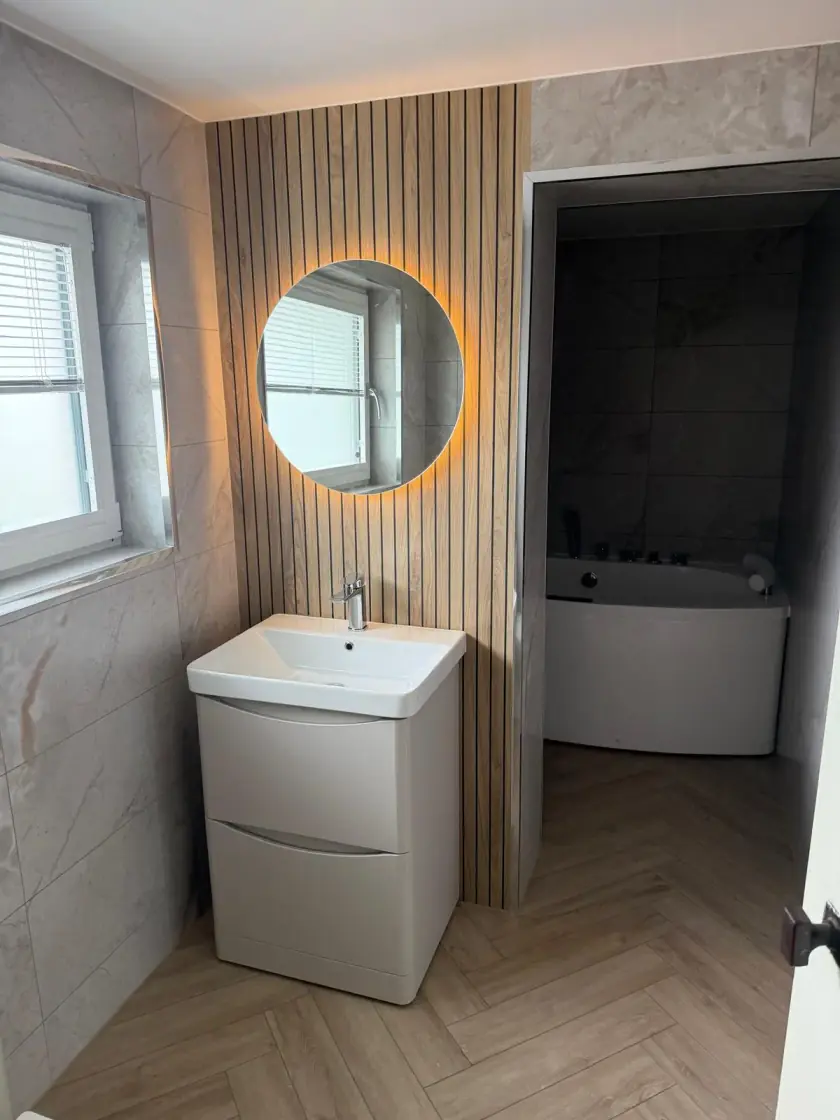 Bathroom vanity set against a vertical wood-slat feature wall with illuminated round mirror